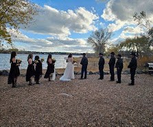 A wedding party sharing a moment beside Rainbow Lake under the trees