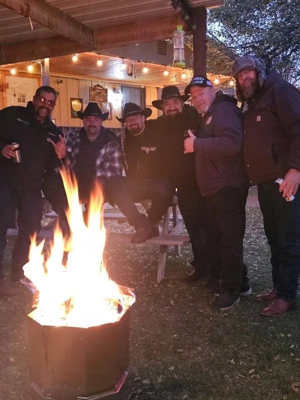 A group of guests gathered around a glowing outdoor fire beneath string lights