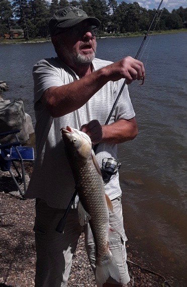 An angler with a fishing rod and his catch along the lakeshore